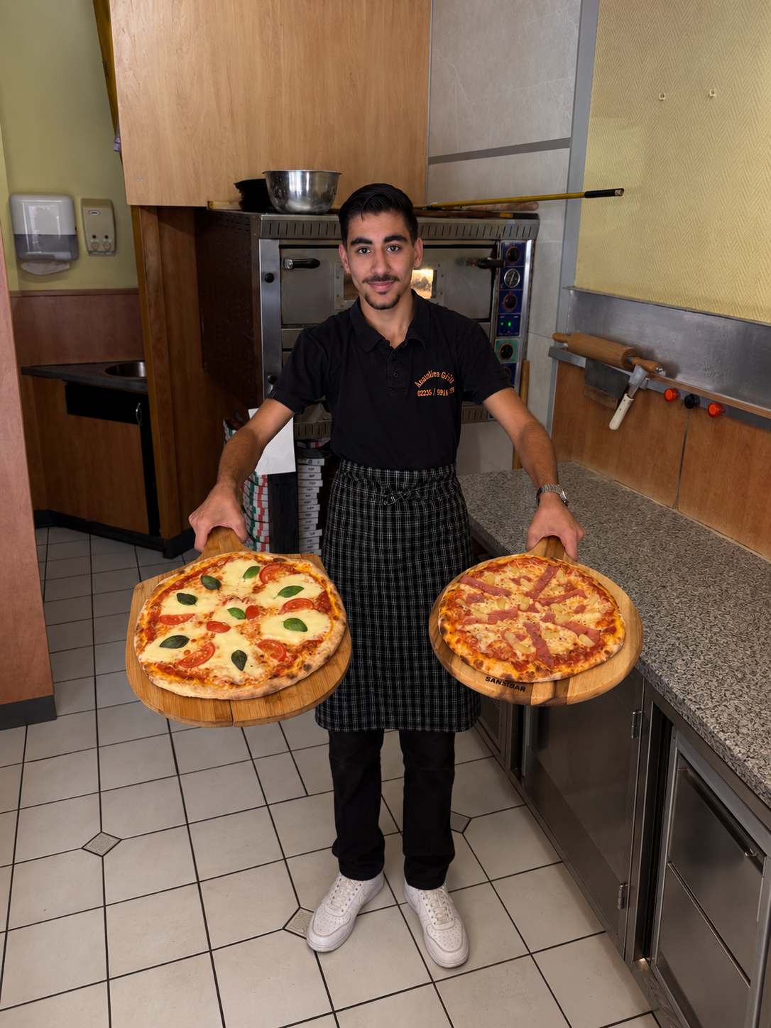 Sohn des Inhabers präsentiert zwei frisch gebackene Pizzen in der Küche