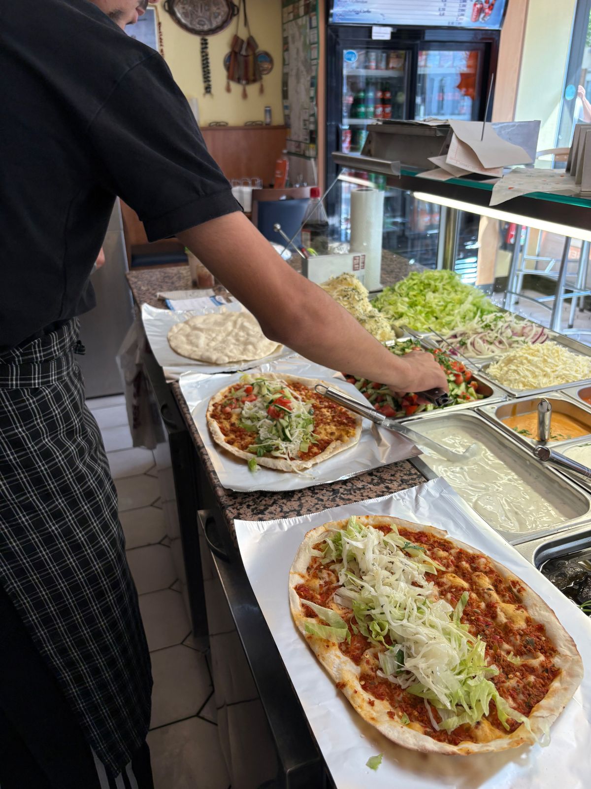 Mitarbeiter belegt Lahmacun mit frischem Salat an der Theke